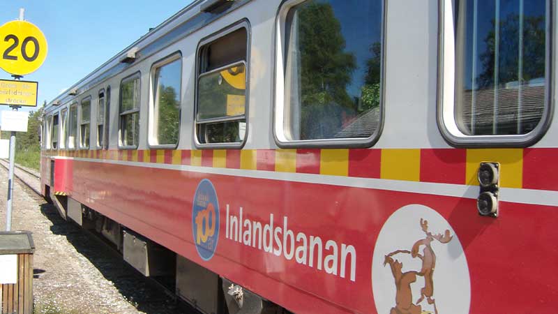 Närbild på Inlandsbanans röda tåg – klassisk svensk rälsbuss mot norr genom skogar och vildmark. Följ med Tjörnarpsbuss på en tur