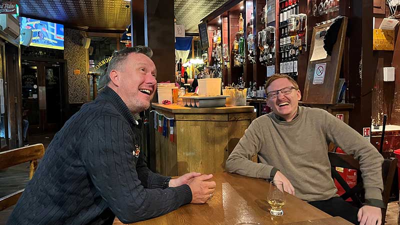 Två glada resenärer njuter av skotsk pubkultur med whisky och skratt – whiskyresan går med Tjörnarpsbuss