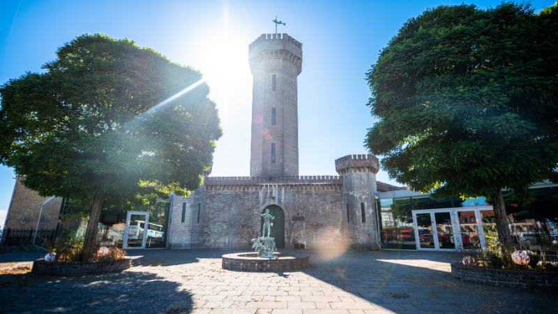 Vattenborgen i Karlskrona, historisk byggnad med torn och borgliknande murar, fontän i förgrunden och grönskande träd under en solig dag.