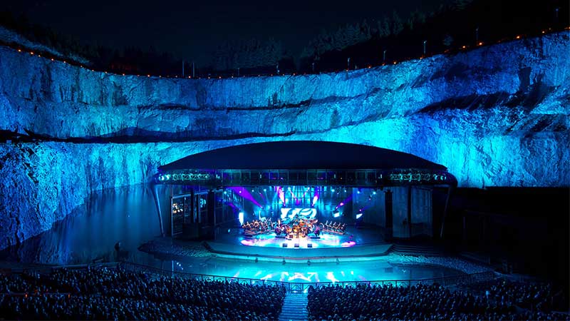 Dalhalla i kvällsljus med upplyst scen, omgiven av dramatiska kalkstensväggar och spegelblank sjö