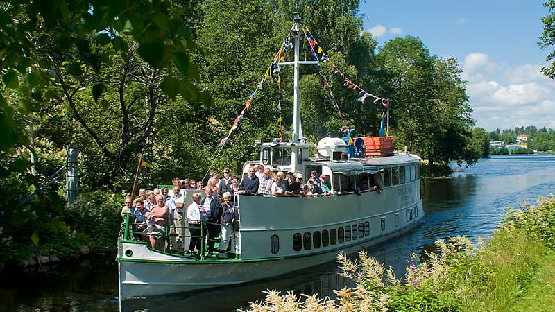 Kanalbåt på tur passerar Mustadfors under sommaren längs Dalslands kanal – rundresa med Tjörnarpsbuss