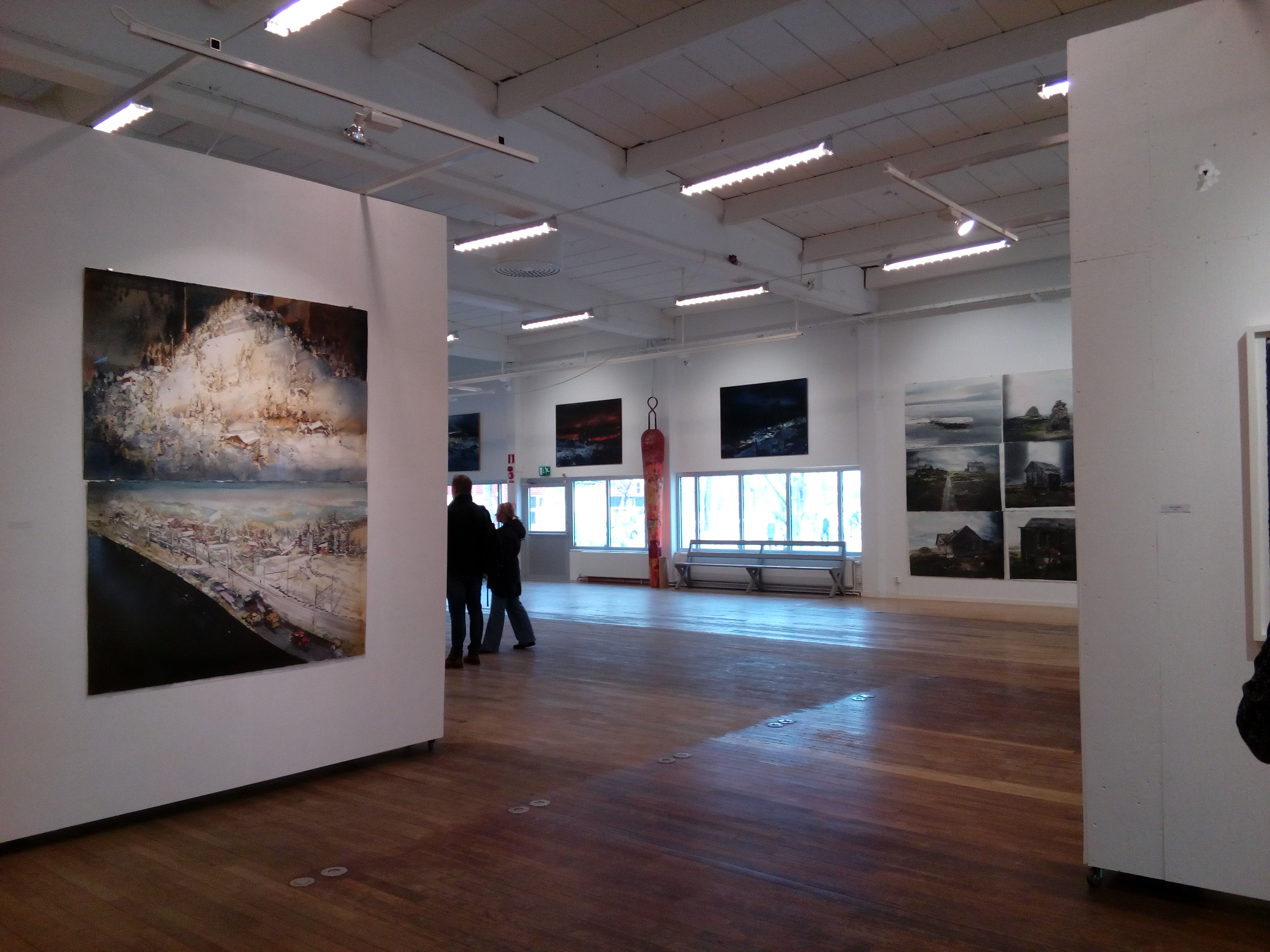 Interiör från Lars Lerins konsthall Sandgrund i Karlstad med stora akvarellmålningar på vita väggar. Ljust galleri med trägolv, högt tak och besökare som betraktar konstverken.